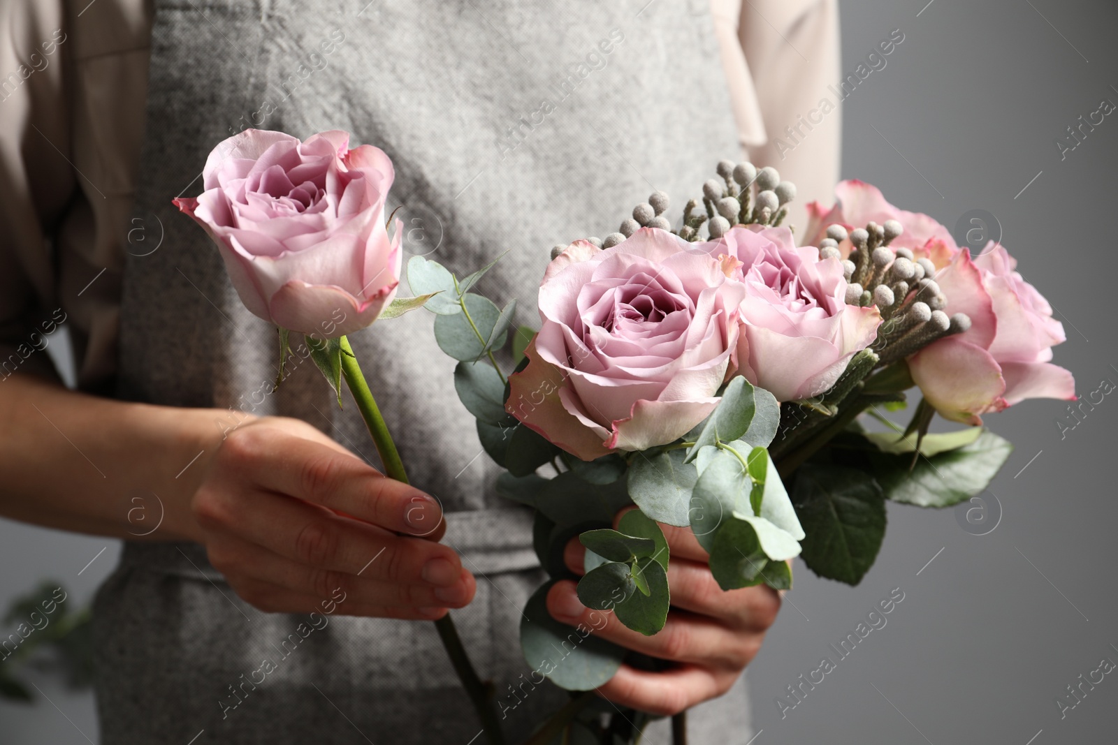 Photo of Florist creating beautiful bouquet with roses indoors, closeup