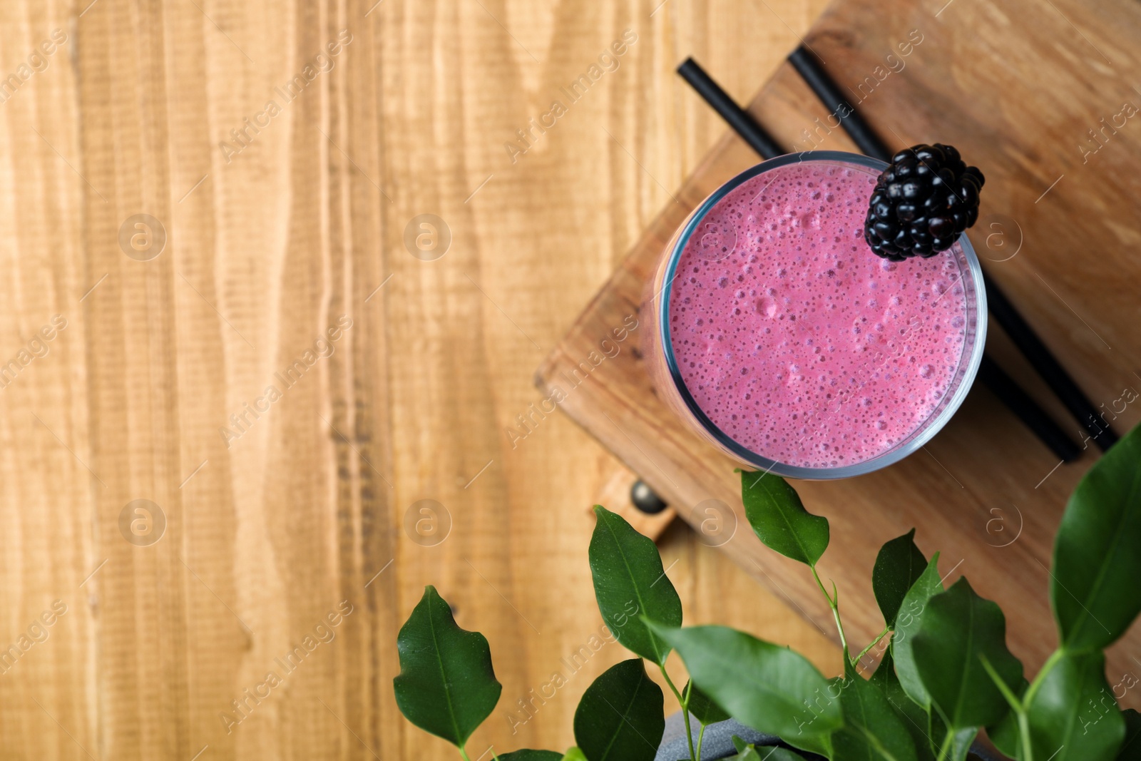 Photo of Glass of blackberry smoothie and green leaves on wooden table, flat lay. Space for text