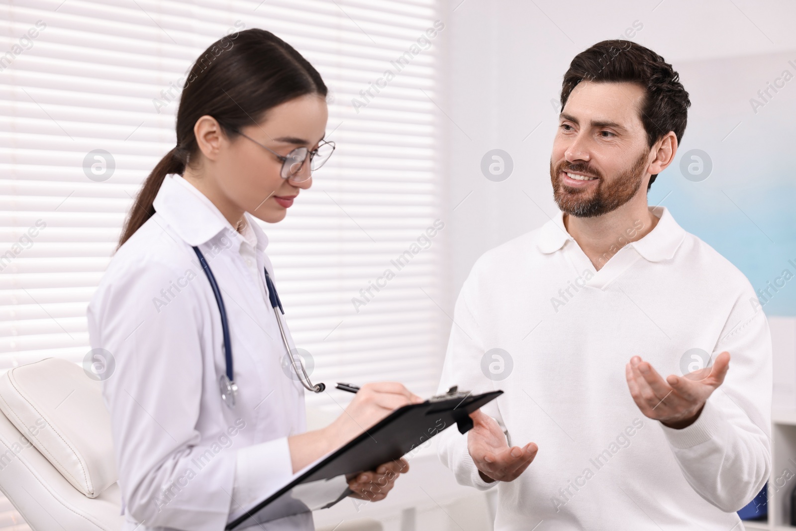 Photo of Doctor with clipboard consulting patient during appointment in clinic