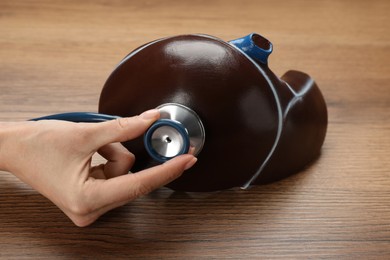 Photo of Doctor with stethoscope examining liver model at wooden table, closeup
