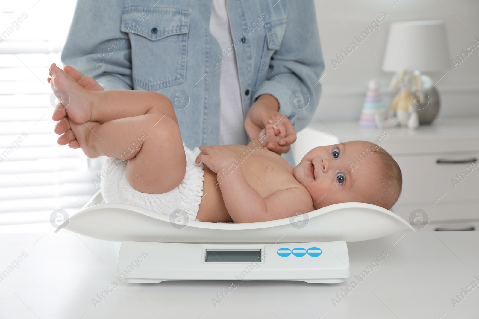 Photo of Young woman weighting her cute baby at home, closeup. Health care