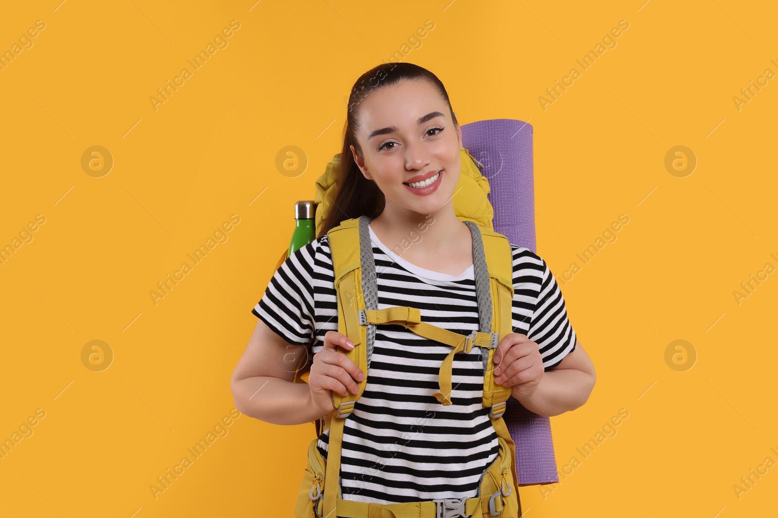 Photo of Smiling young woman with backpack on orange background. Active tourism