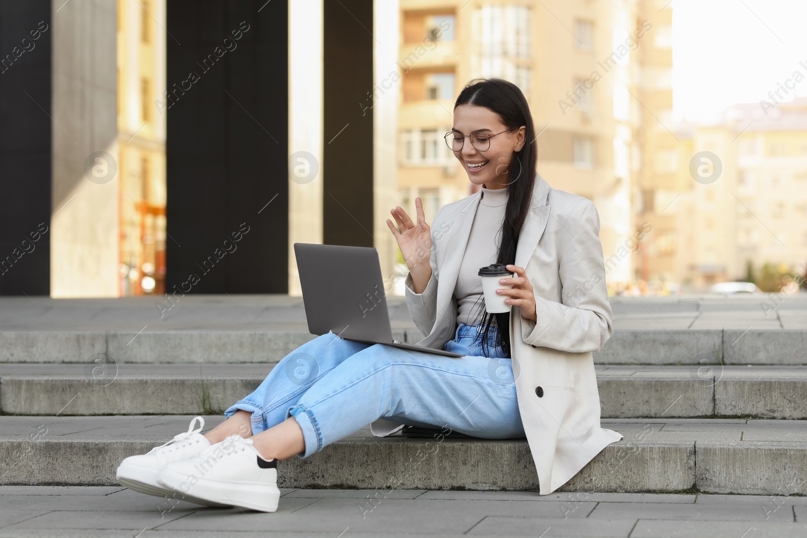 Photo of Happy young woman using modern laptop for video call on stairs outdoors