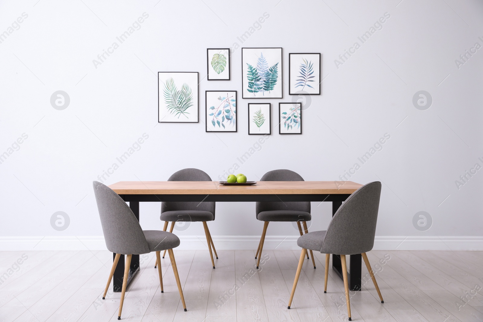 Photo of Stylish room interior with modern table, chairs and paintings of tropical leaves. Idea for design