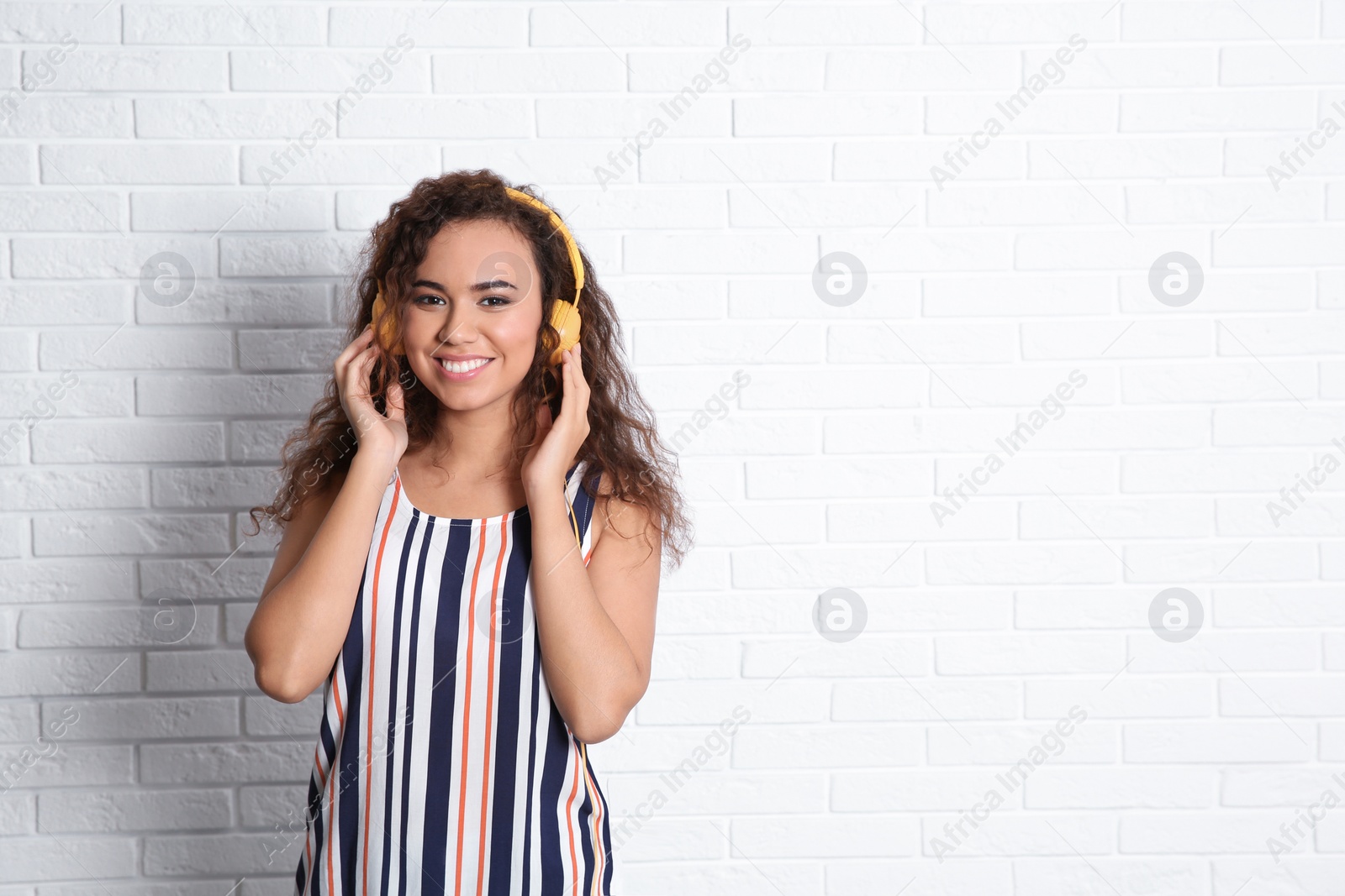 Photo of African-American woman listening to music with headphones near brick wall, space for text