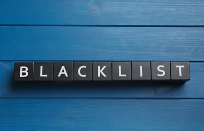 Black cubes with word Blacklist on blue wooden table, flat lay