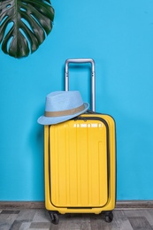 Bright yellow suitcase with hat and tropical leaf near color wall indoors