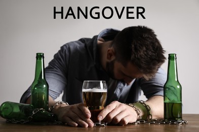 Image of Suffering from hangover. Man chained to glass of beer at table