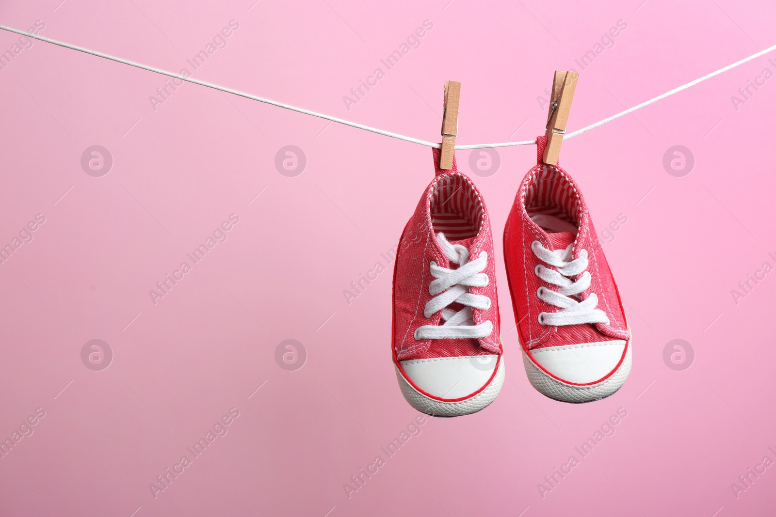 Photo of Cute small shoes hanging on washing line against color background, space for text. Baby accessories