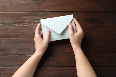 Woman with white paper envelope at wooden table, top view