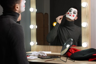 Photo of Young man applying mime makeup near mirror in dressing room