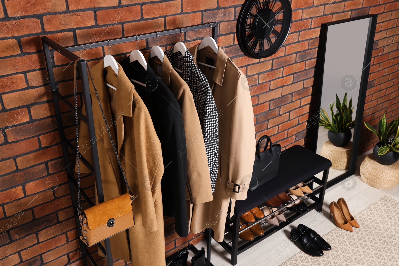 Photo of Stylish hallway with coat rack and shoe storage bench near brick wall. Interior design