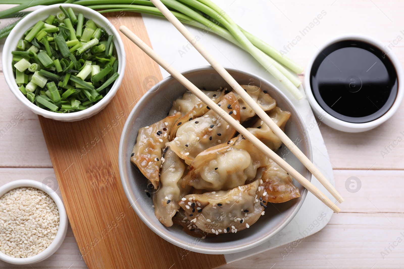 Photo of Delicious gyoza (asian dumplings), soy sauce, green onion and sesame on white wooden table, flat lay