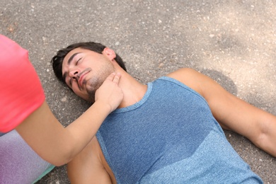 Photo of Young woman checking pulse of unconscious man on street