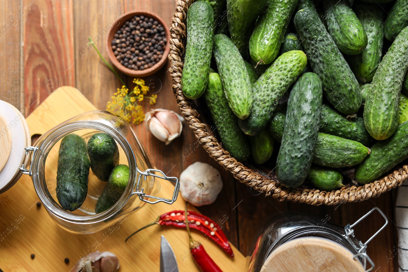 Photo of Fresh cucumbers, other ingredients and jars on wooden table, flat lay. Pickling vegetables