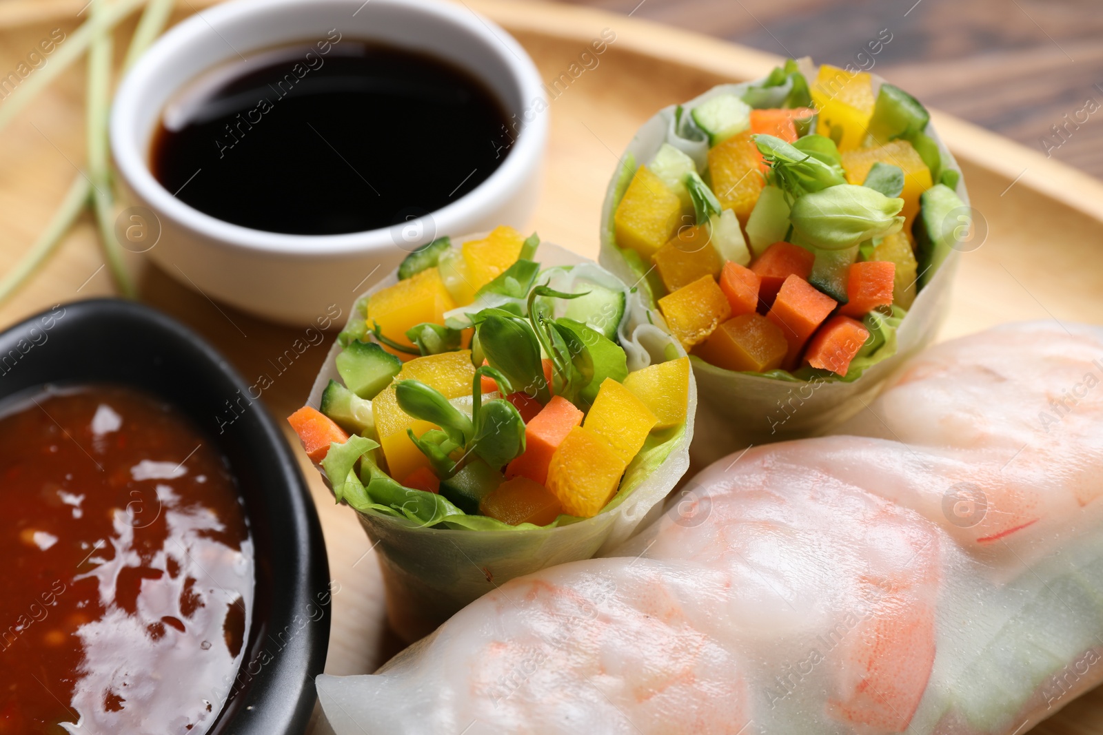 Photo of Tasty spring rolls and sauces on wooden plate, closeup