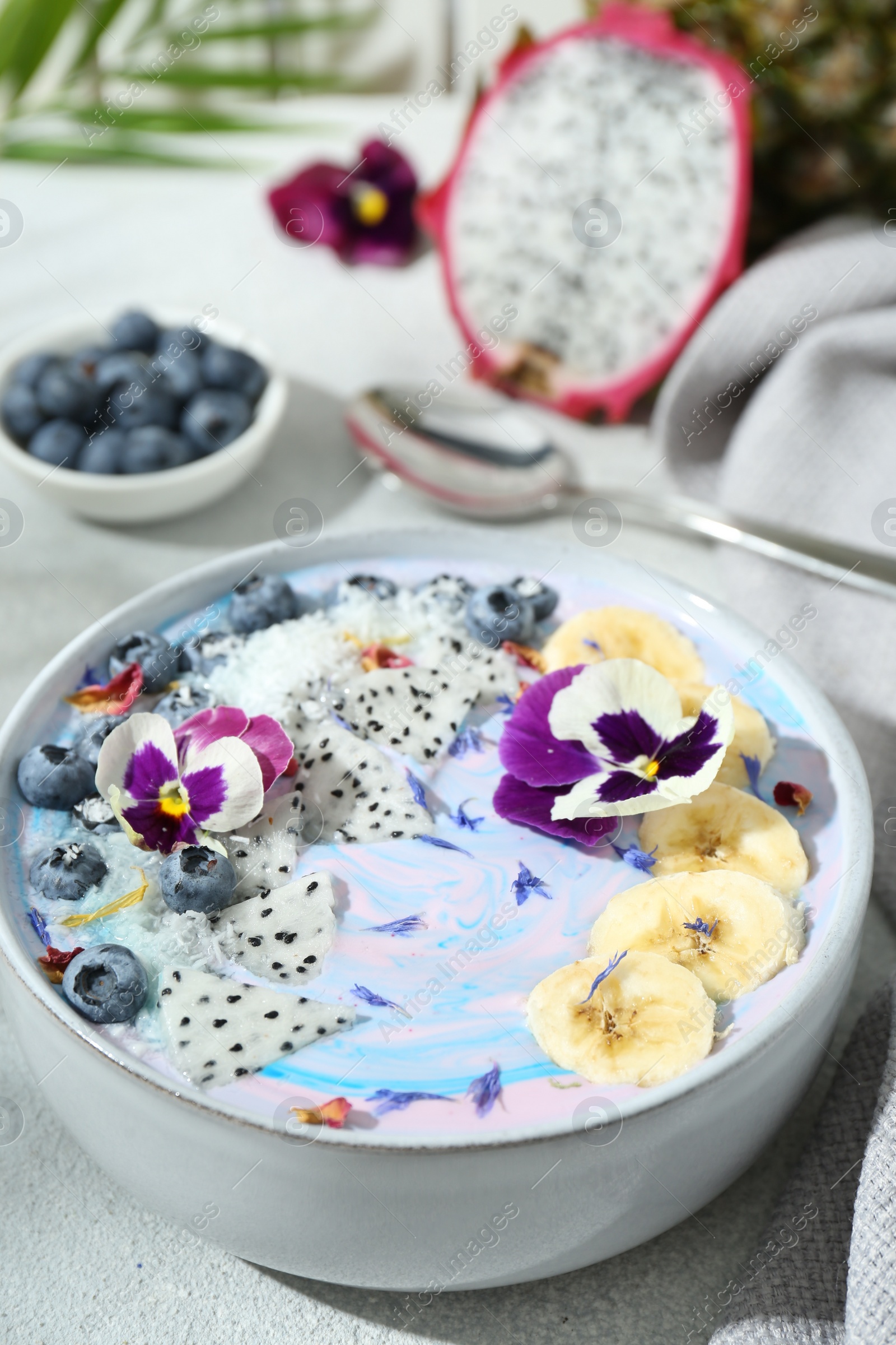 Photo of Delicious smoothie bowl with fresh fruits, blueberries and flowers on light grey table, closeup