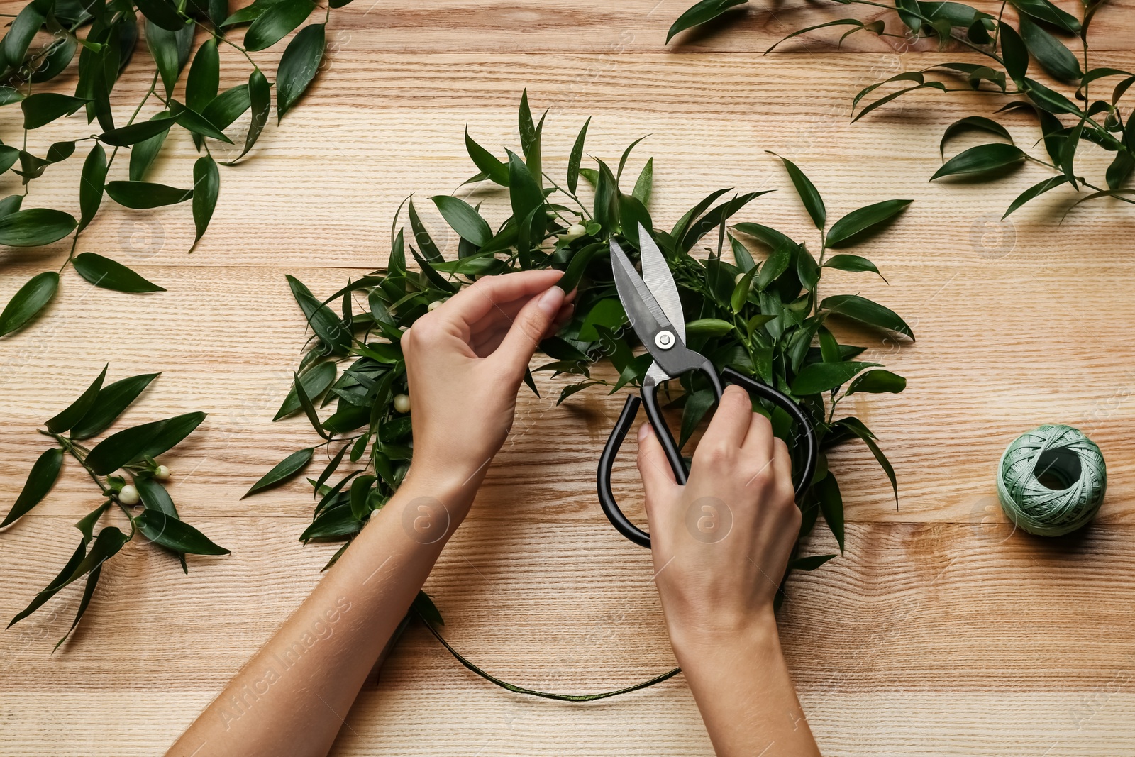 Photo of Florist making beautiful mistletoe wreath at wooden table, top view. Traditional Christmas decor