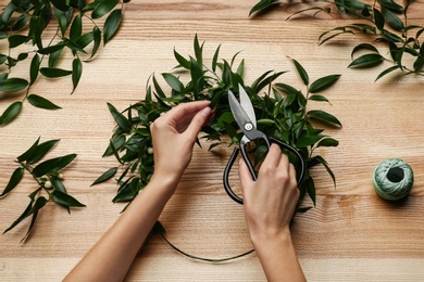 Florist making beautiful mistletoe wreath at wooden table, top view. Traditional Christmas decor