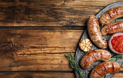 Photo of Tasty grilled sausages served on wooden table, flat lay. Space for text