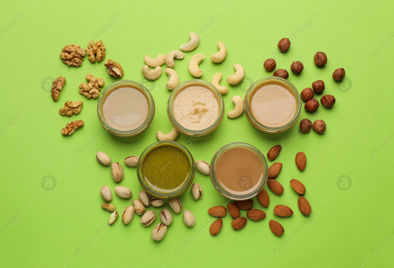 Photo of Different types of delicious nut butters and ingredients on light green background, flat lay