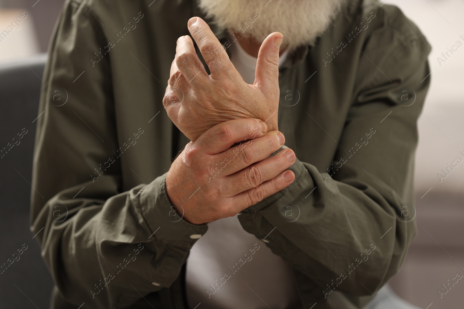 Photo of Senior man suffering from pain in hand on blurred background, closeup. Rheumatism symptom