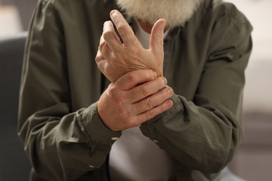 Senior man suffering from pain in hand on blurred background, closeup. Rheumatism symptom