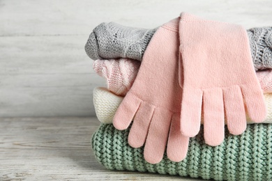 Photo of Stacked sweaters and gloves on wooden table, closeup. Autumn clothes