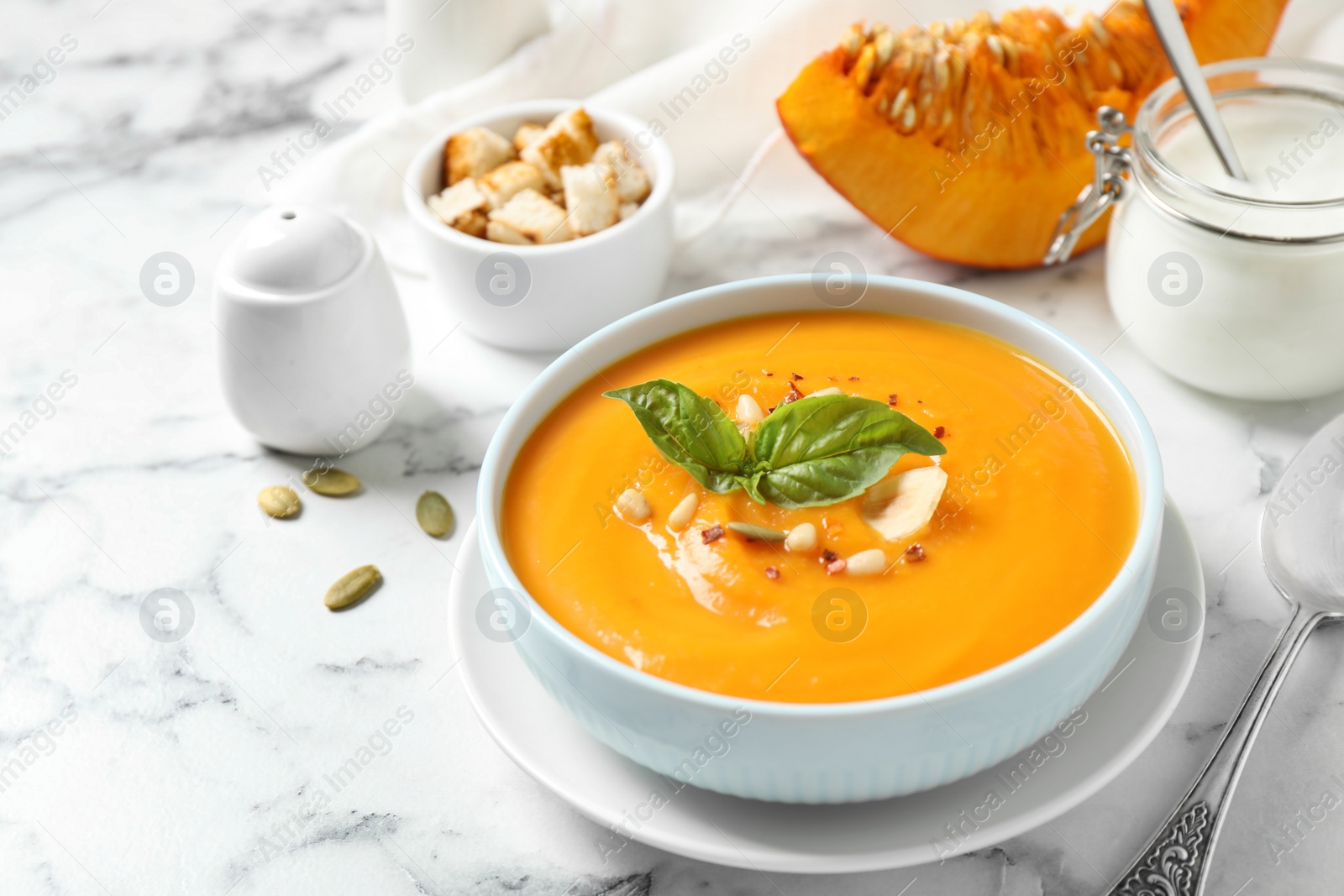 Photo of Delicious pumpkin soup in bowl on marble table