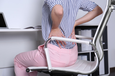 Photo of Woman with lower back pain sitting in office chair at table, closeup