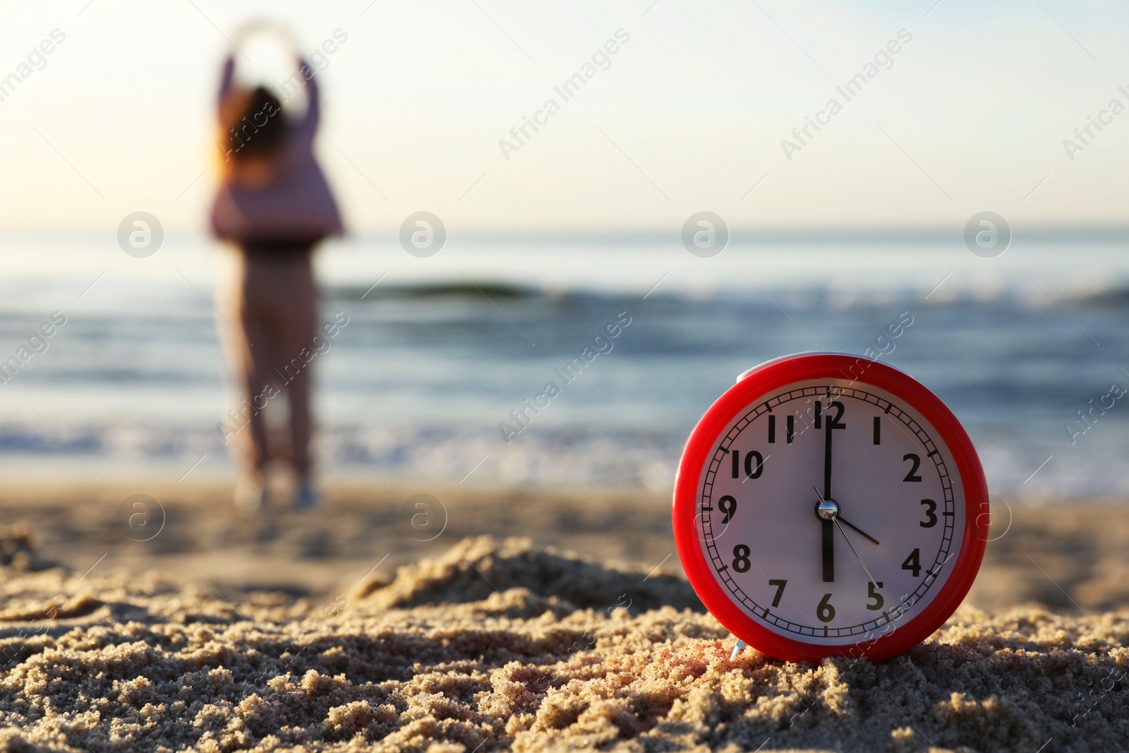 Photo of Woman doing morning exercises near river outdoors, focus on alarm clock