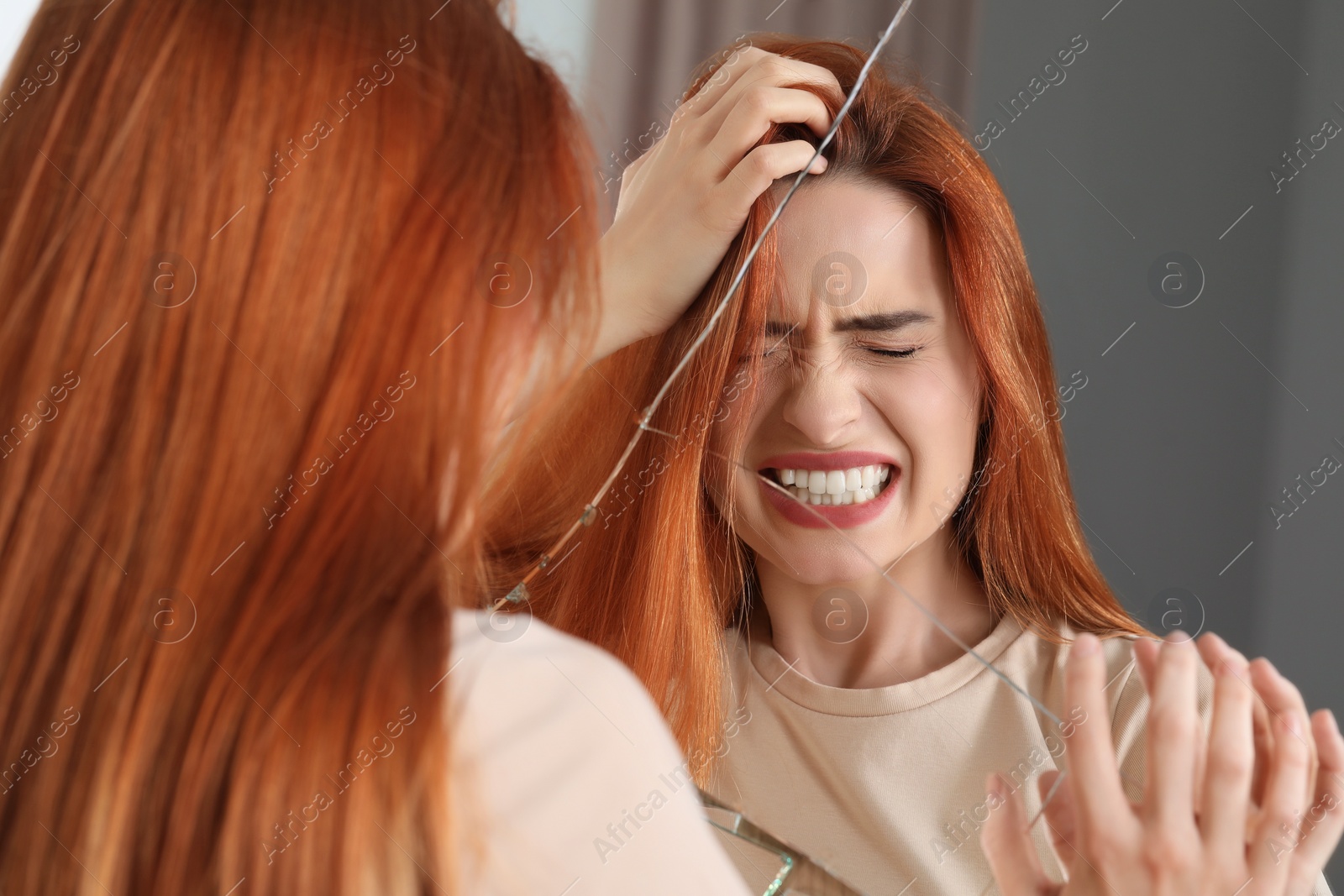 Photo of Emotional young woman suffering from mental problems near broken mirror indoors