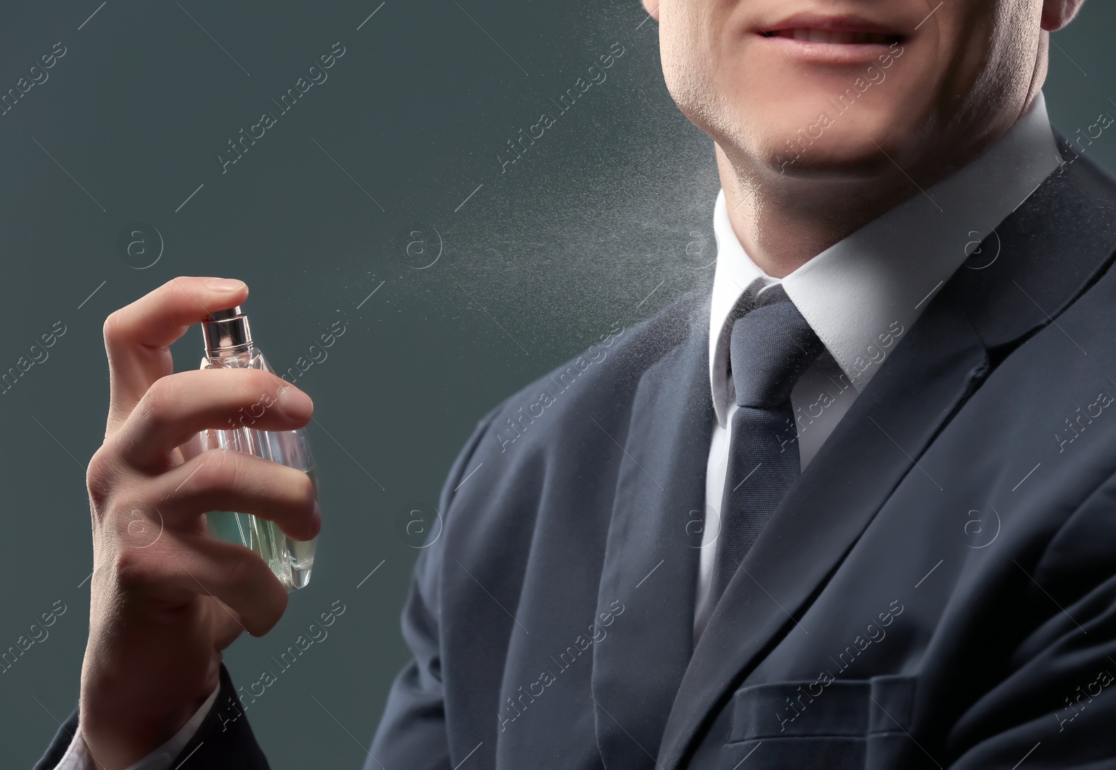 Photo of Handsome man in suit using perfume on dark background, closeup