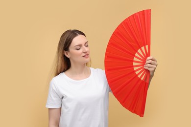 Photo of Beautiful woman waving red hand fan to cool herself on beige background