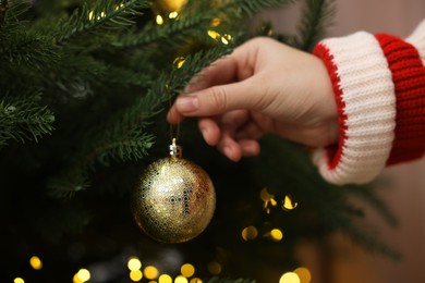 Photo of Woman decorating fir tree with golden Christmas ball indoors, closeup