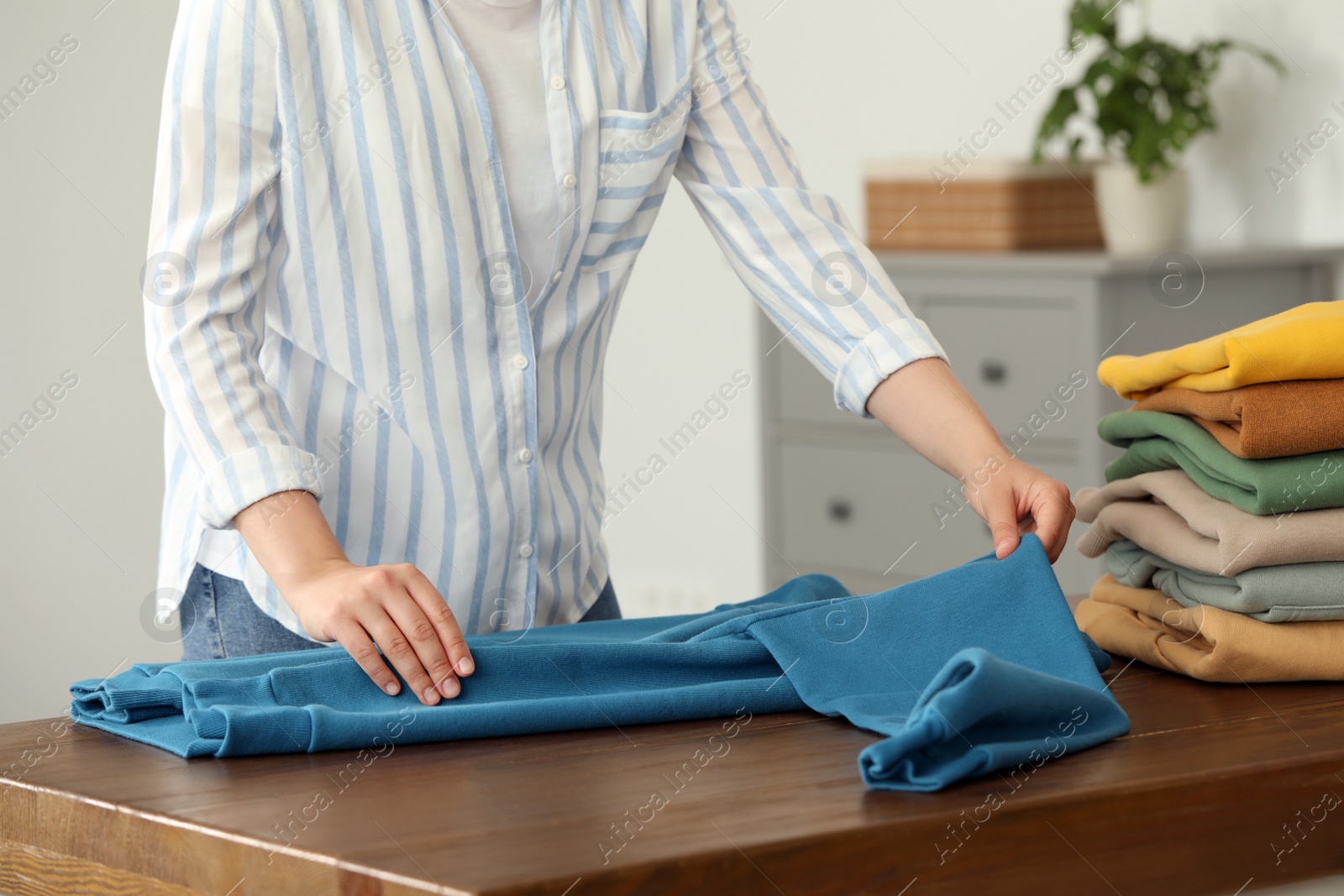 Photo of Woman folding clothes at wooden table indoors, closeup