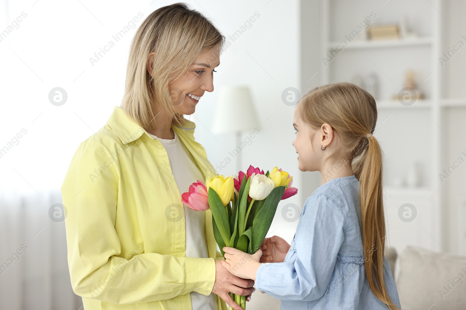 Photo of Little daughter congratulating her mom with bouquet of tulips at home. Happy Mother's Day