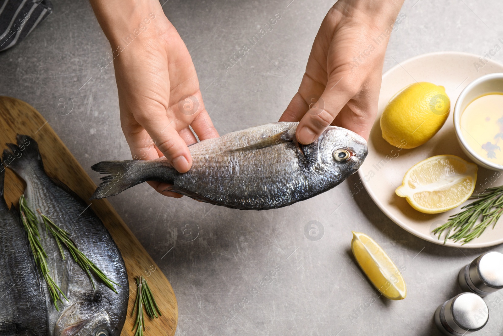 Photo of Woman holding dorada fish over grey table, top view