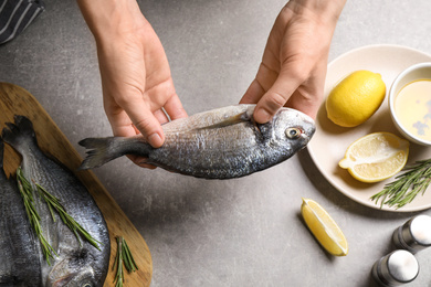 Photo of Woman holding dorada fish over grey table, top view