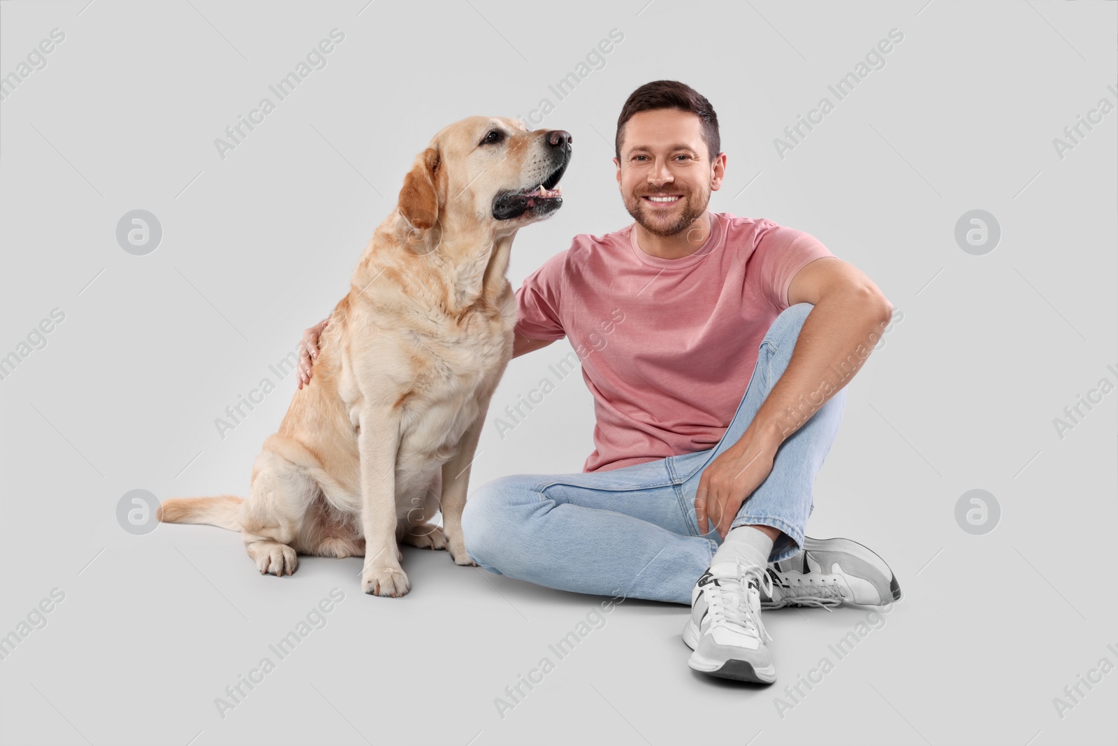 Photo of Man hugging with adorable Labrador Retriever dog on light gray background. Lovely pet