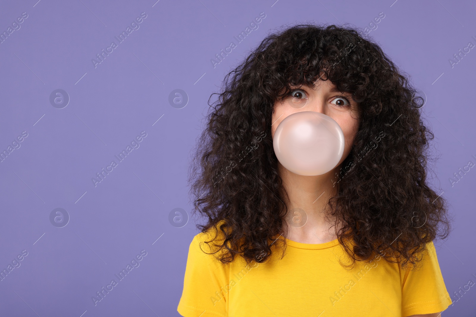 Photo of Beautiful young woman blowing bubble gum on purple background. Space for text
