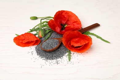 Spoon of poppy seeds and flowers on white wooden table