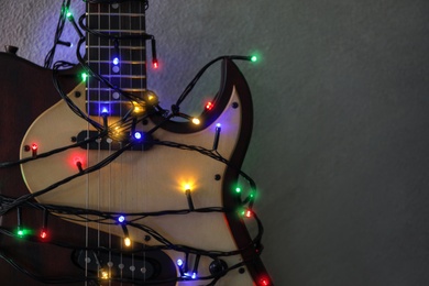 Photo of Guitar with colorful lights on grey stone background, space for text. Christmas music
