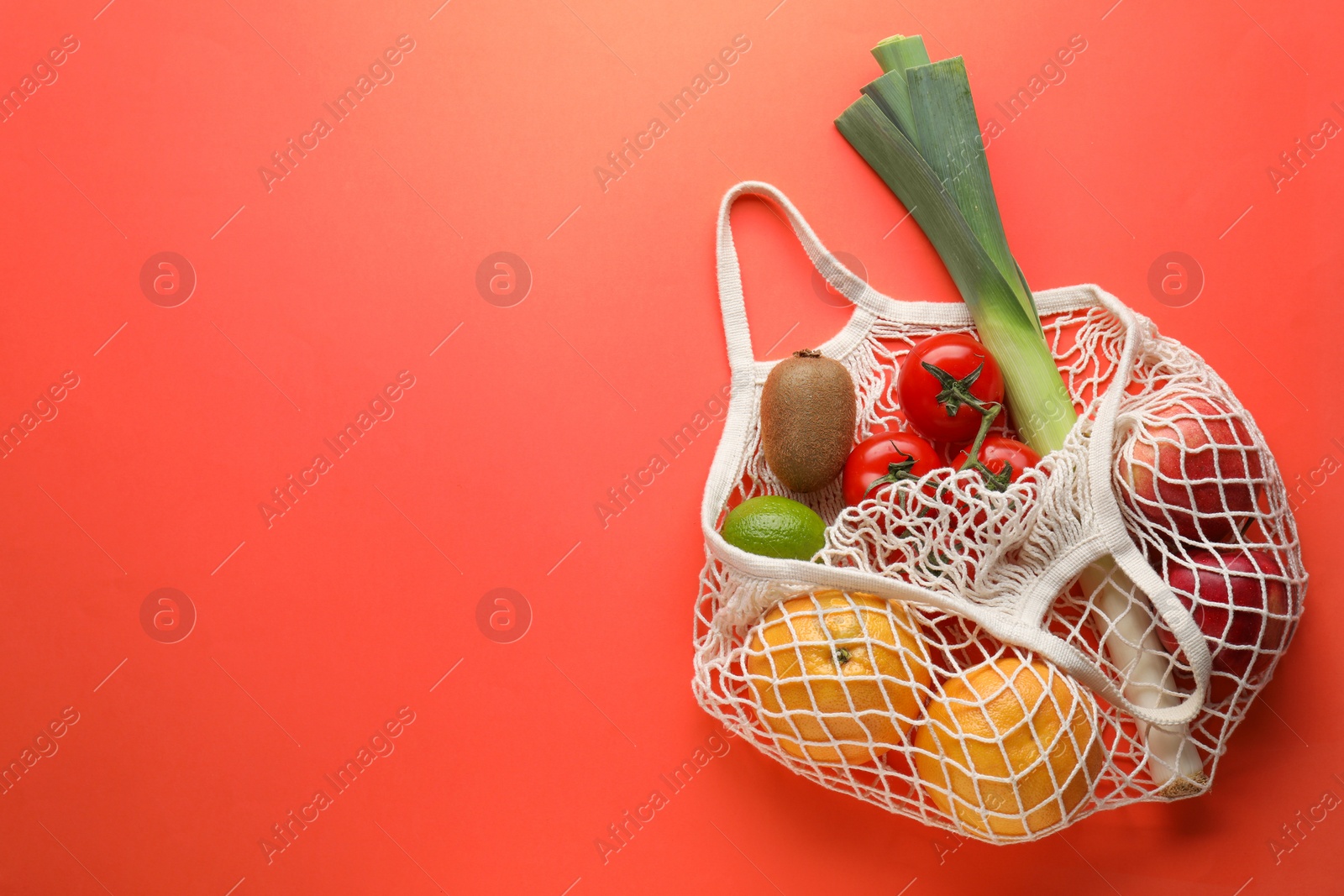 Photo of String bag with different vegetables and fruits on red background, top view. Space for text