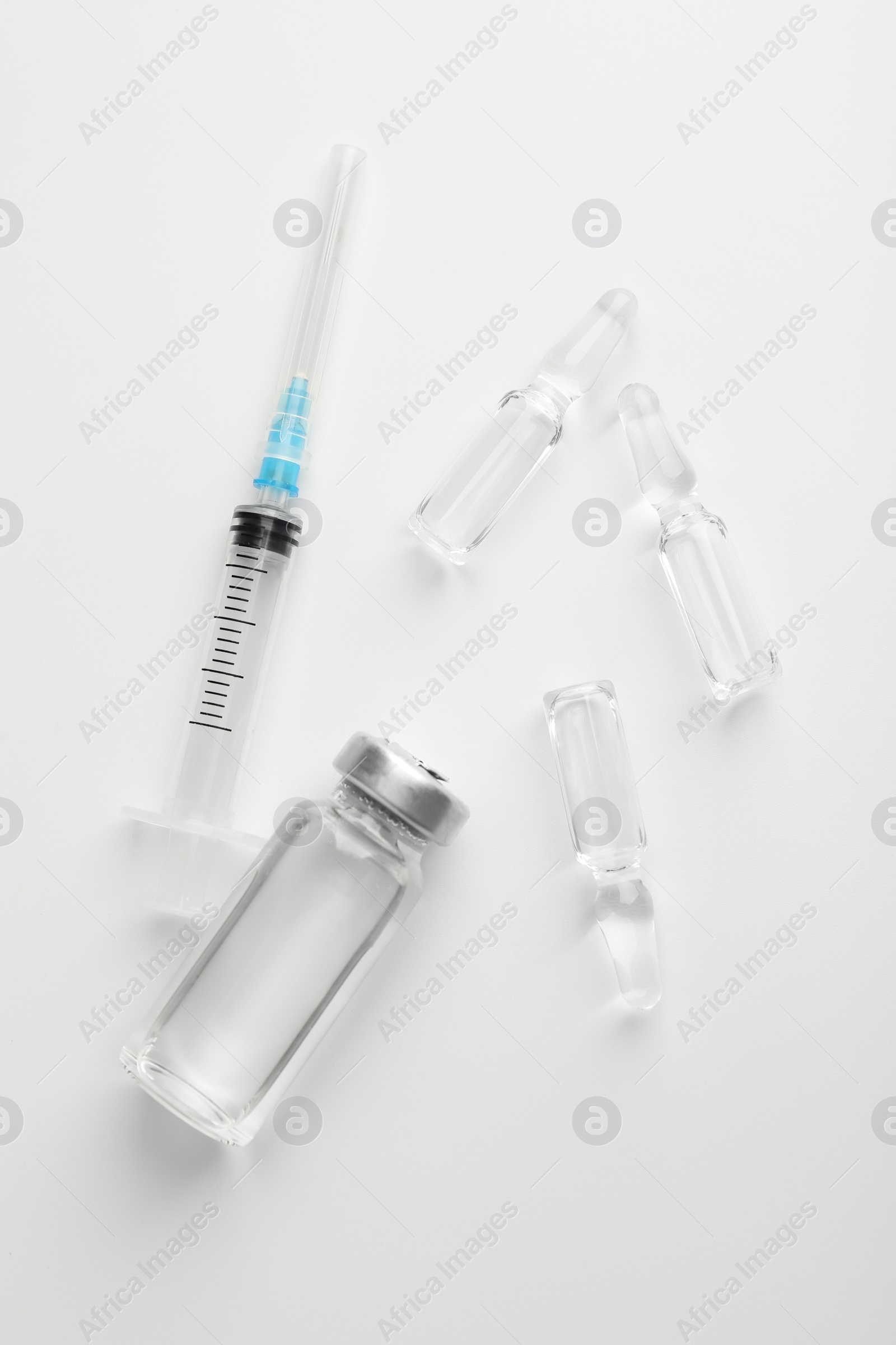 Photo of Glass ampoules with liquid and syringe on white background, flat lay