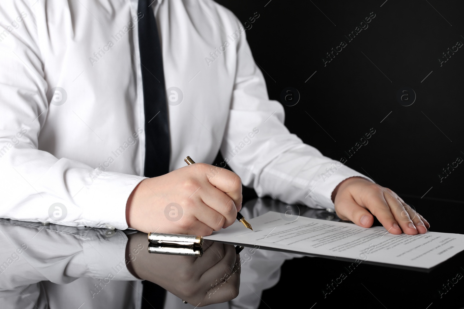 Photo of Notary signing document at black table, closeup