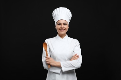 Happy female chef with wooden spoon on black background