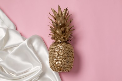 Photo of Golden pineapple and white silk fabric on pink background, top view. Space for text