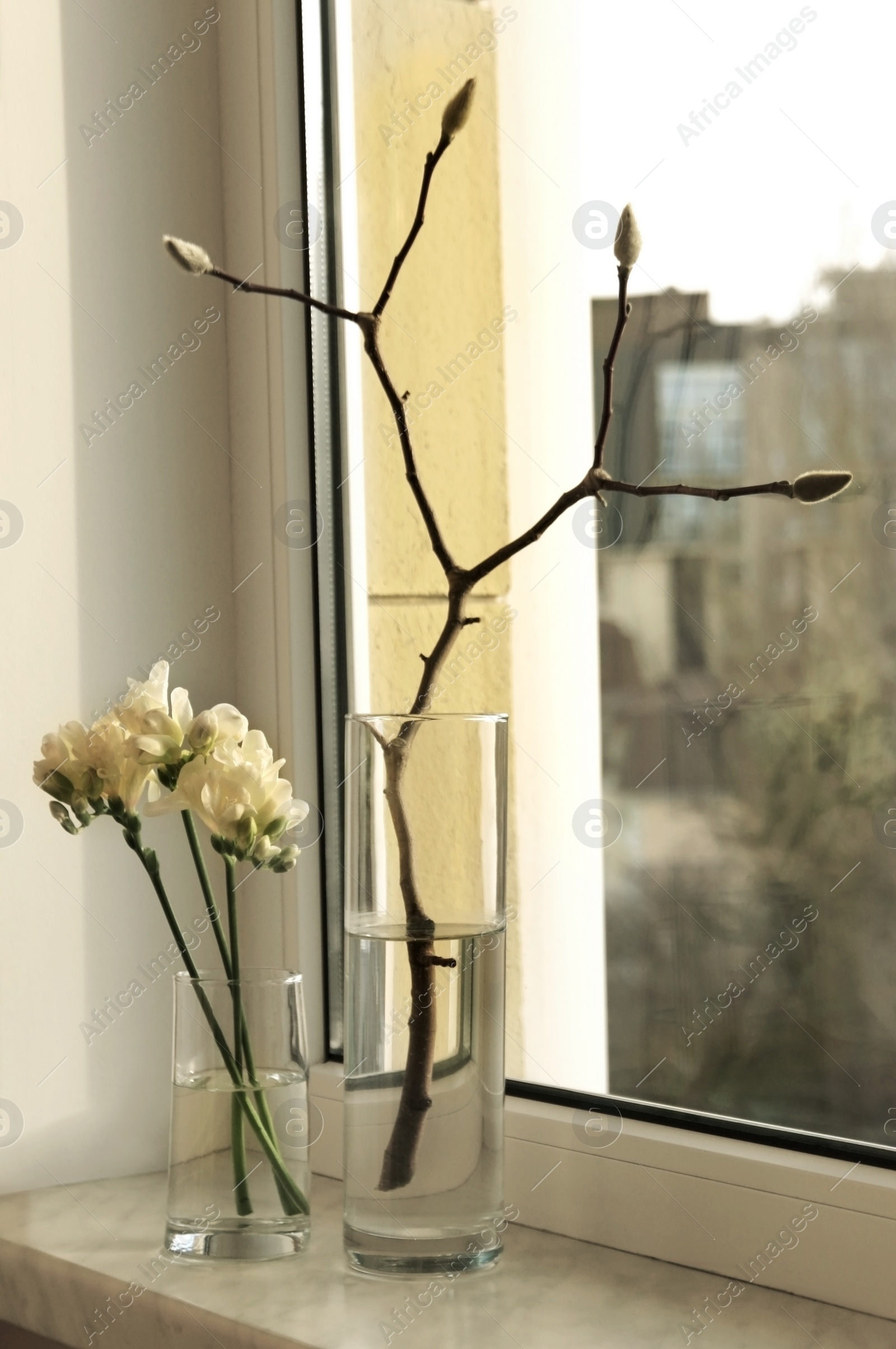 Photo of Beautiful freesia flowers and tree branch with buds on window sill indoors. Spring time