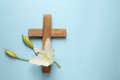 Wooden cross and lily flowers on light blue background, top view with space for text. Easter attributes